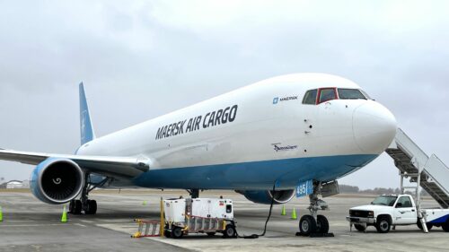 A Maersk Air Cargo airplane is parked on an airport tarmac under overcast skies. The aircraft has its nose painted in white with “MAERSK AIR CARGO” written on the fuselage. Ground support equipment and stairs are positioned next to the plane, capturing a scene likely to be featured in June Air Cargo News.