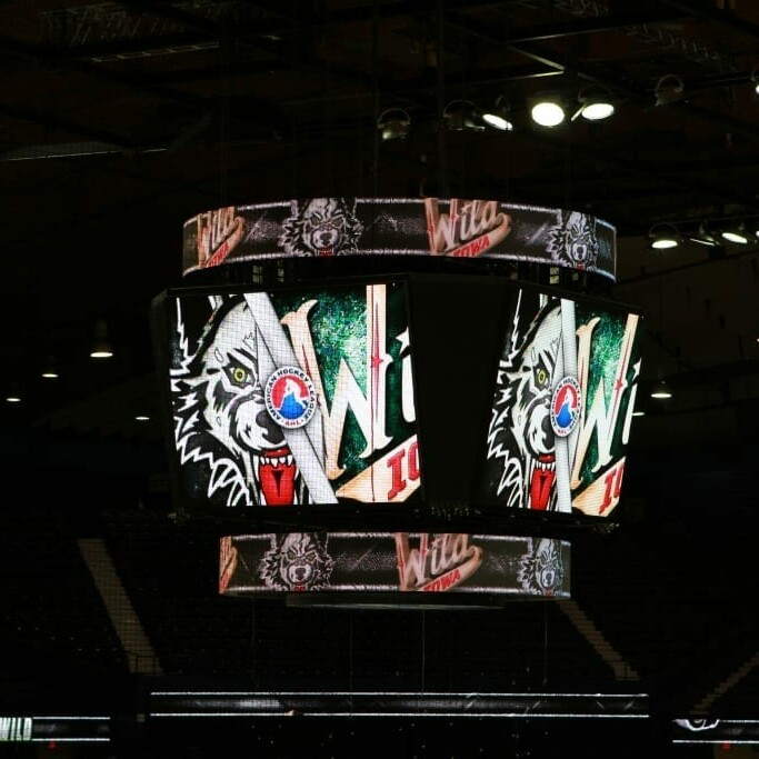 A large electronic scoreboard at an indoor sports arena displays the logo and text "Wilderness," with a prominent wolf graphic reminiscent of the Chicago Wolves. The seating areas in the background are empty, as lights illuminate the display during the 2018 March Networking Night.