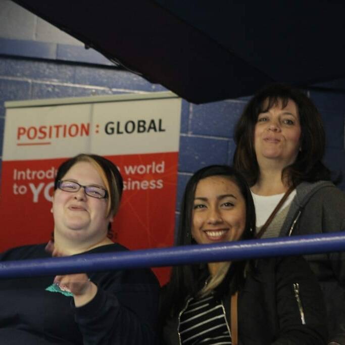 Three people are smiling while posing on an indoor balcony. Behind them are banners with text promoting networking and global business, suggesting a Networking Night event. They seem to be at an event or conference from 2018 March. The background includes a blue wall, evoking the spirit of the Chicago Wolves.