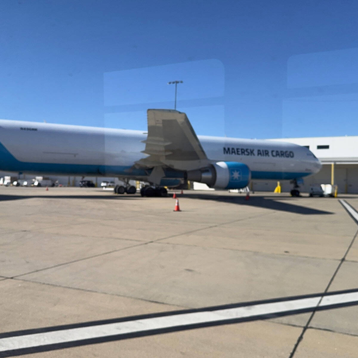 A large cargo airplane with "Maersk Air Cargo" emblazoned on the side is parked on the airport tarmac. The white and blue plane sits amid ground service vehicles under a clear, blue sky, ready for its next journey. Consider a visit to witness the bustling activity firsthand.