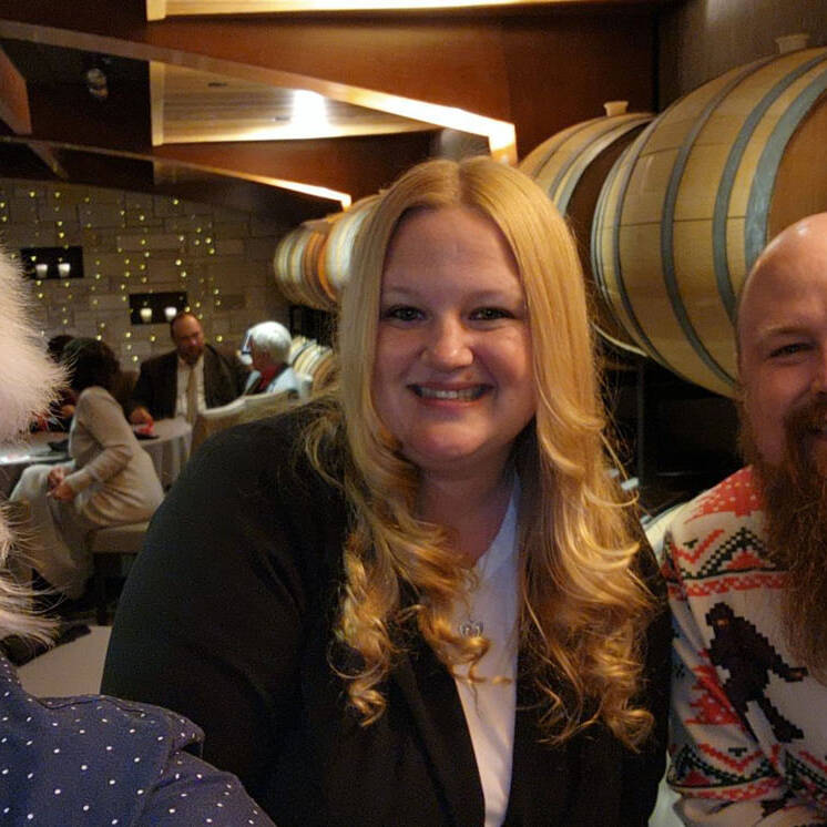 Four people smiling in a festive holiday party setting, with large wooden barrels in the background. The person on the right is sporting a holiday-themed sweater and headband. The cozy atmosphere suggests a cheerful gathering that perfectly captures the spirit of 2024 celebrations.