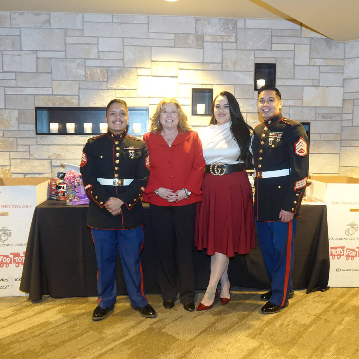 A group of four people, two in Marine uniforms and two in civilian outfits, stand smiling at a 2024 Holiday display for a 