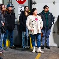 Inside a garage-like setting, a group dressed in winter clothing gathers for a UPS event. A "STOP" sign and speed limit sign are visible, guiding the way for 2024. The yellow lines on the floor neatly outline parking spaces, creating an organized atmosphere.